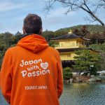 Young Man In An Orange Hoodie With Tourist Japan Branding And The Tagline Japan With Passion, Looking Out At The Golden Pavillion In Kyoto